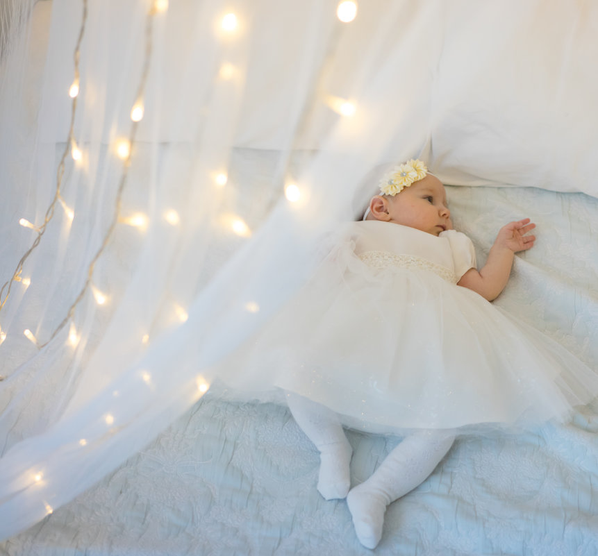 Малышка на кровати с новогодними огоньками в белом платье - Ирина Вайнбранд