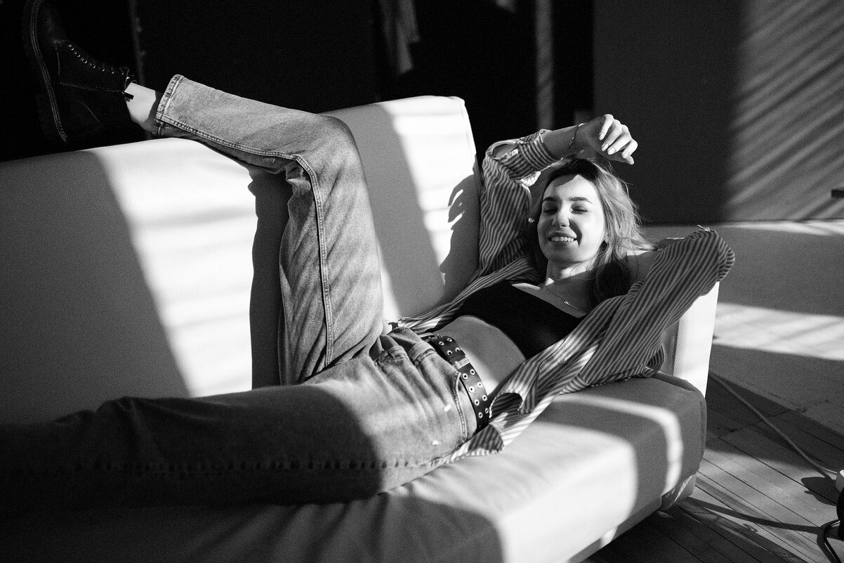 Девушка в джинсах и легкой рубашке лежит на диване под яркими солнечными лучами - Lenar Abdrakhmanov